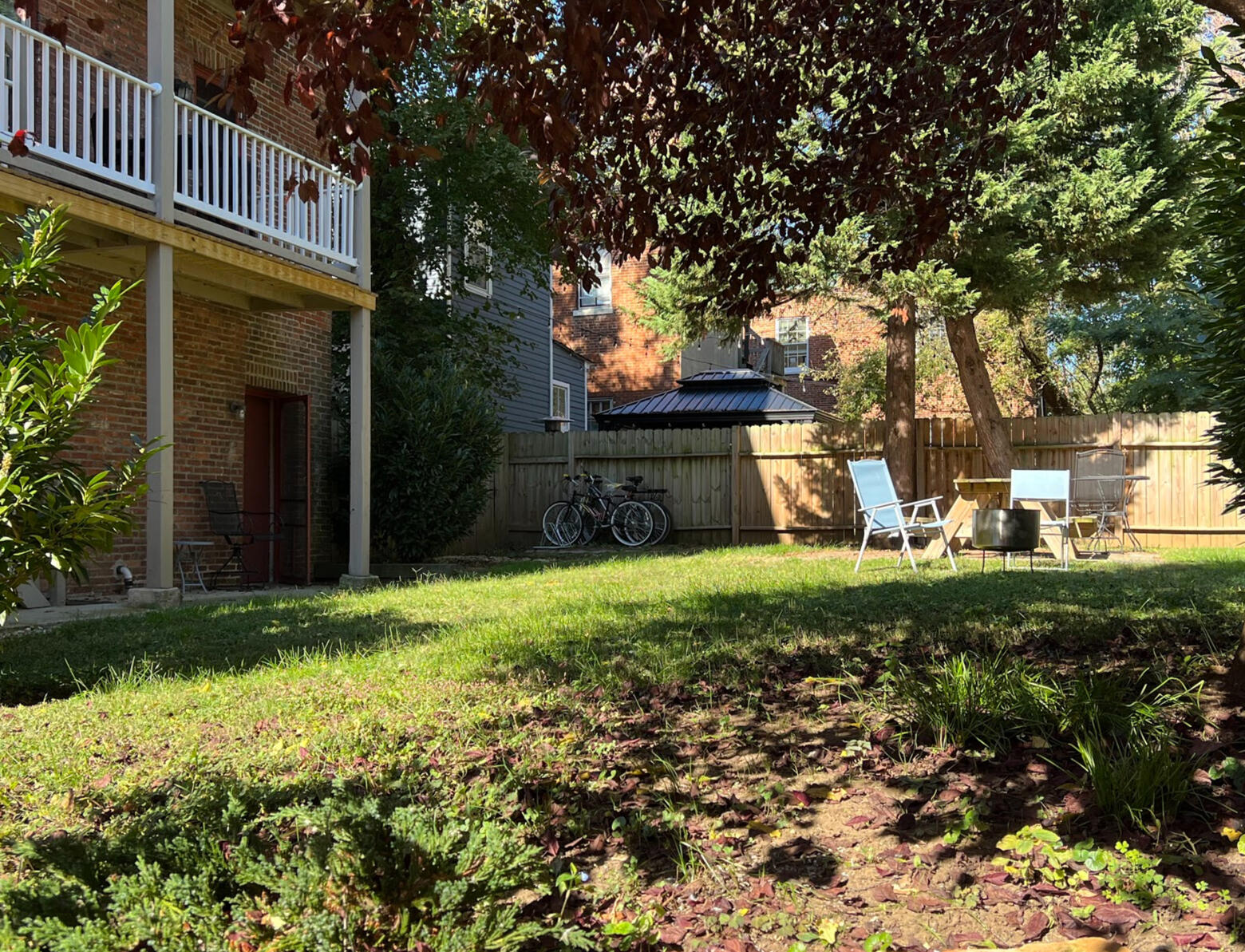 The private fenced garden behind the building, with mature shade trees, seating, and the brick rear elevation