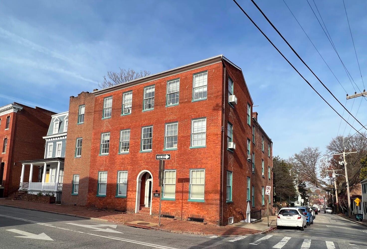 The red-brick corner building at 144 Duke of Gloucester Street under a blue sky, with seafoam-painted window trim and an arched entry